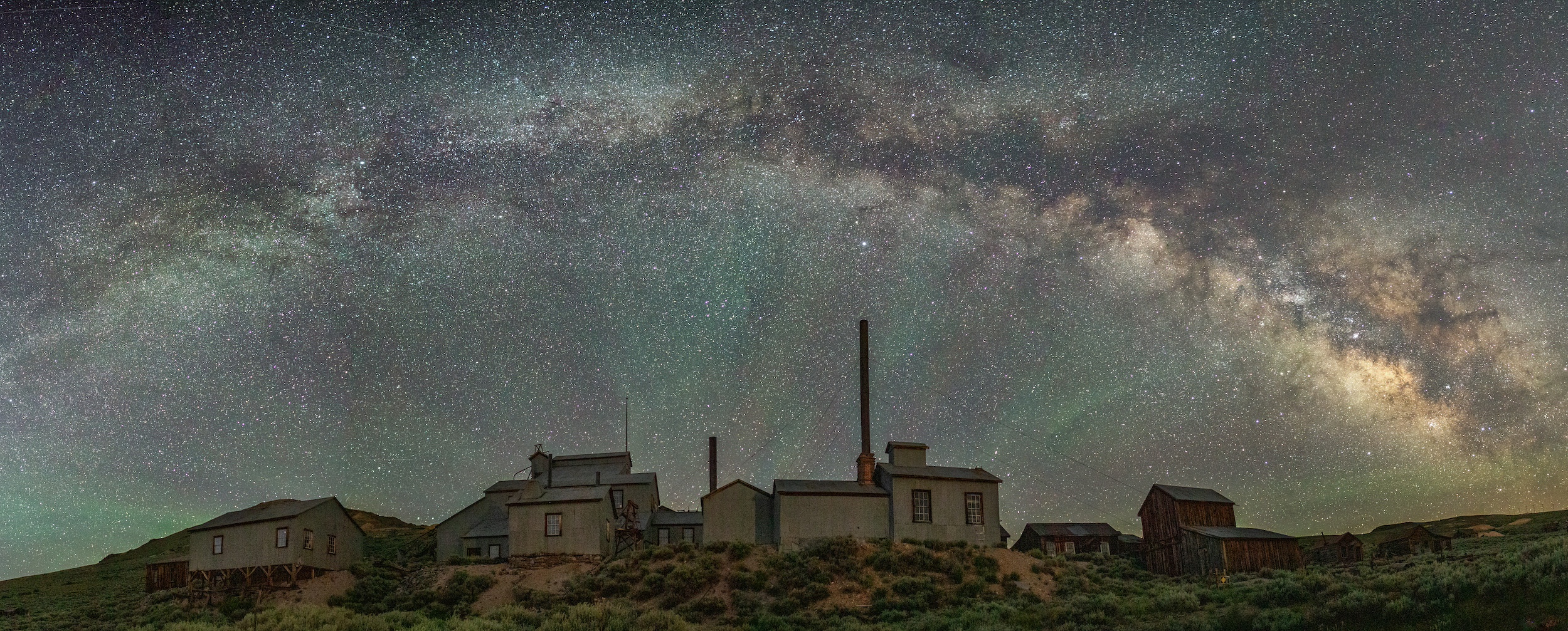 factory smokestacks under a starry night sky crossed by a vivid Milky Way and streaked with glowing green light