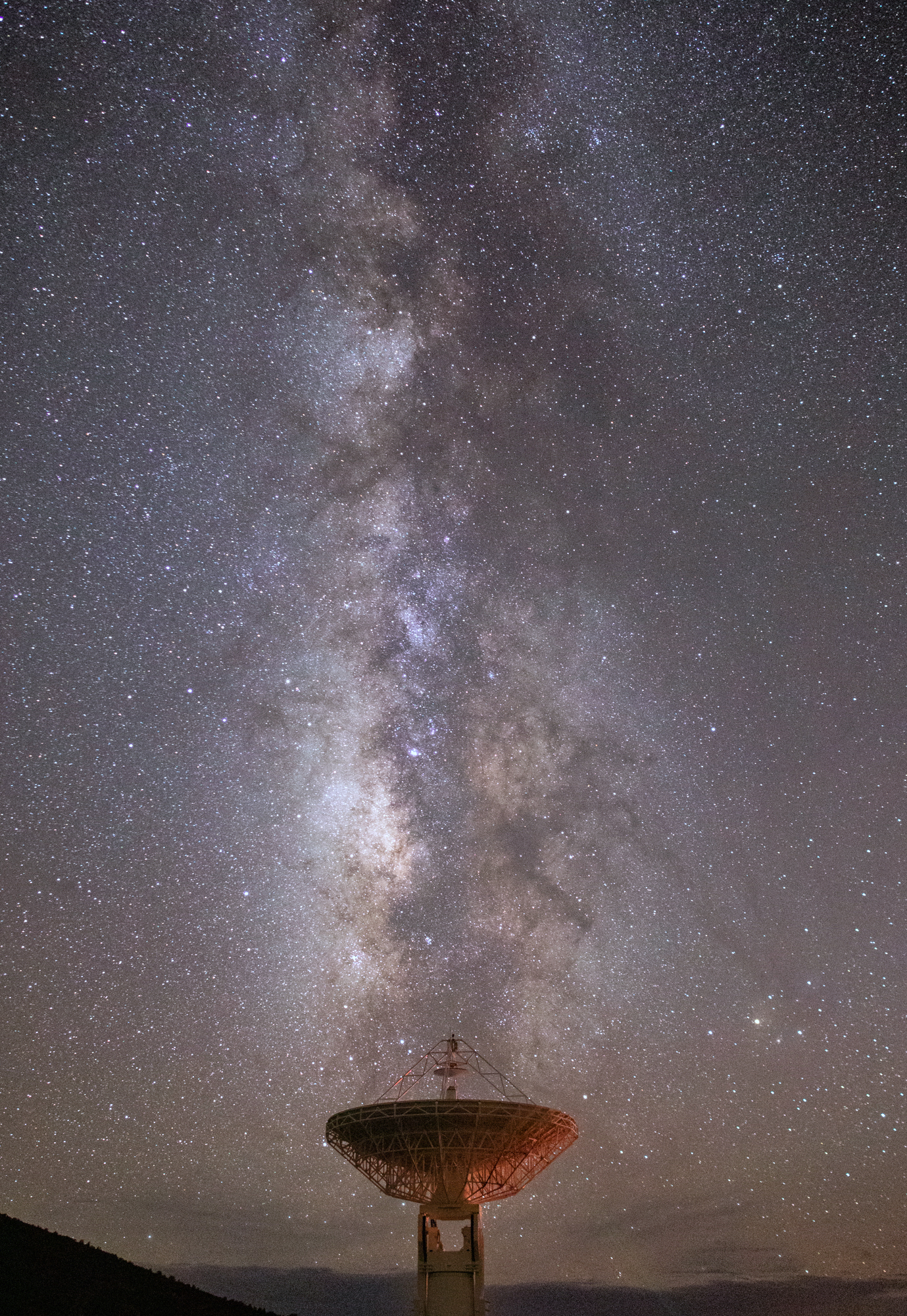 large antenna dish under a night sky with colorful stars and the hazy light of the Milky Way