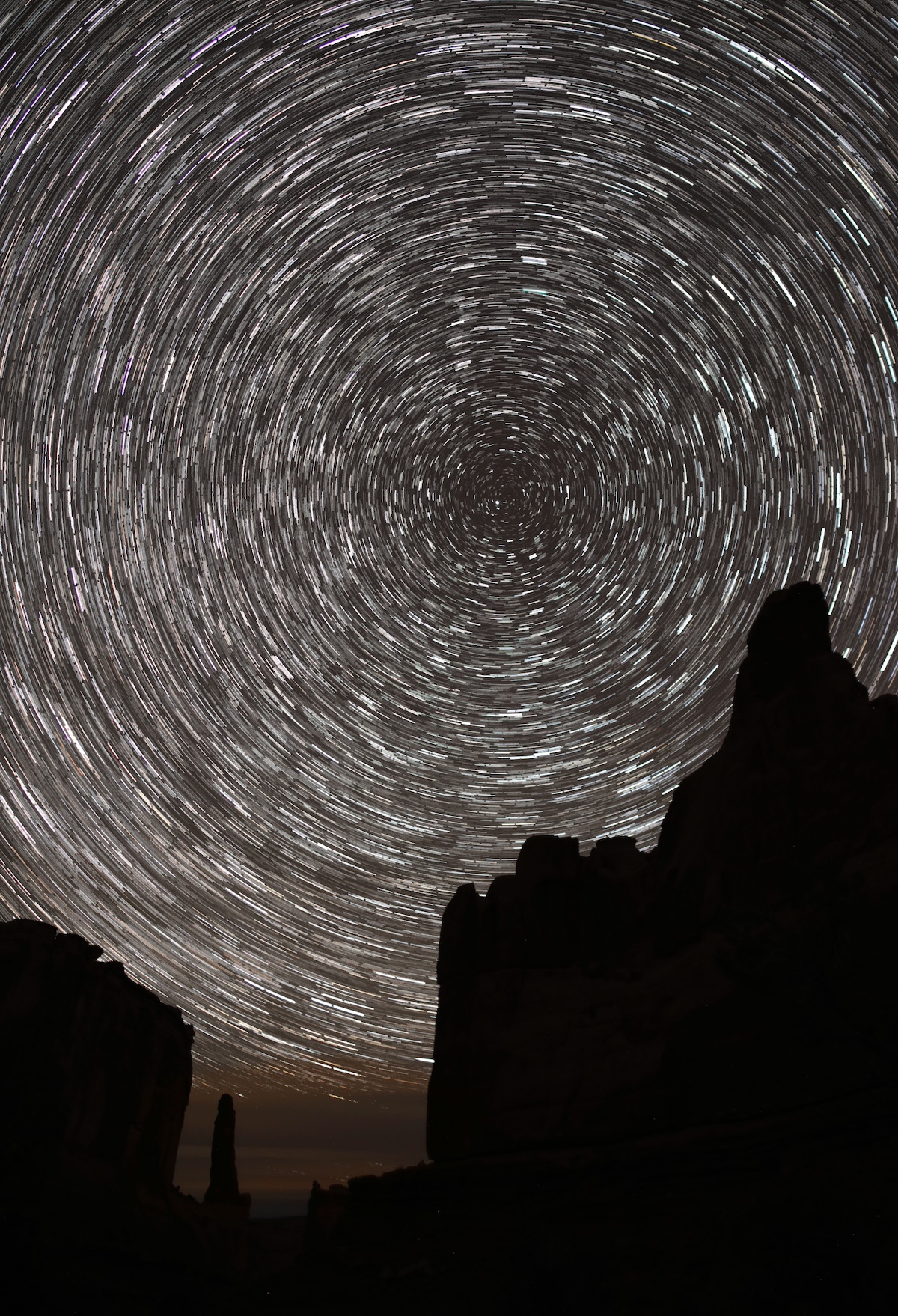 slihouetted towers of sandstone at night. in the sky is a diffuse glow of yellow and red