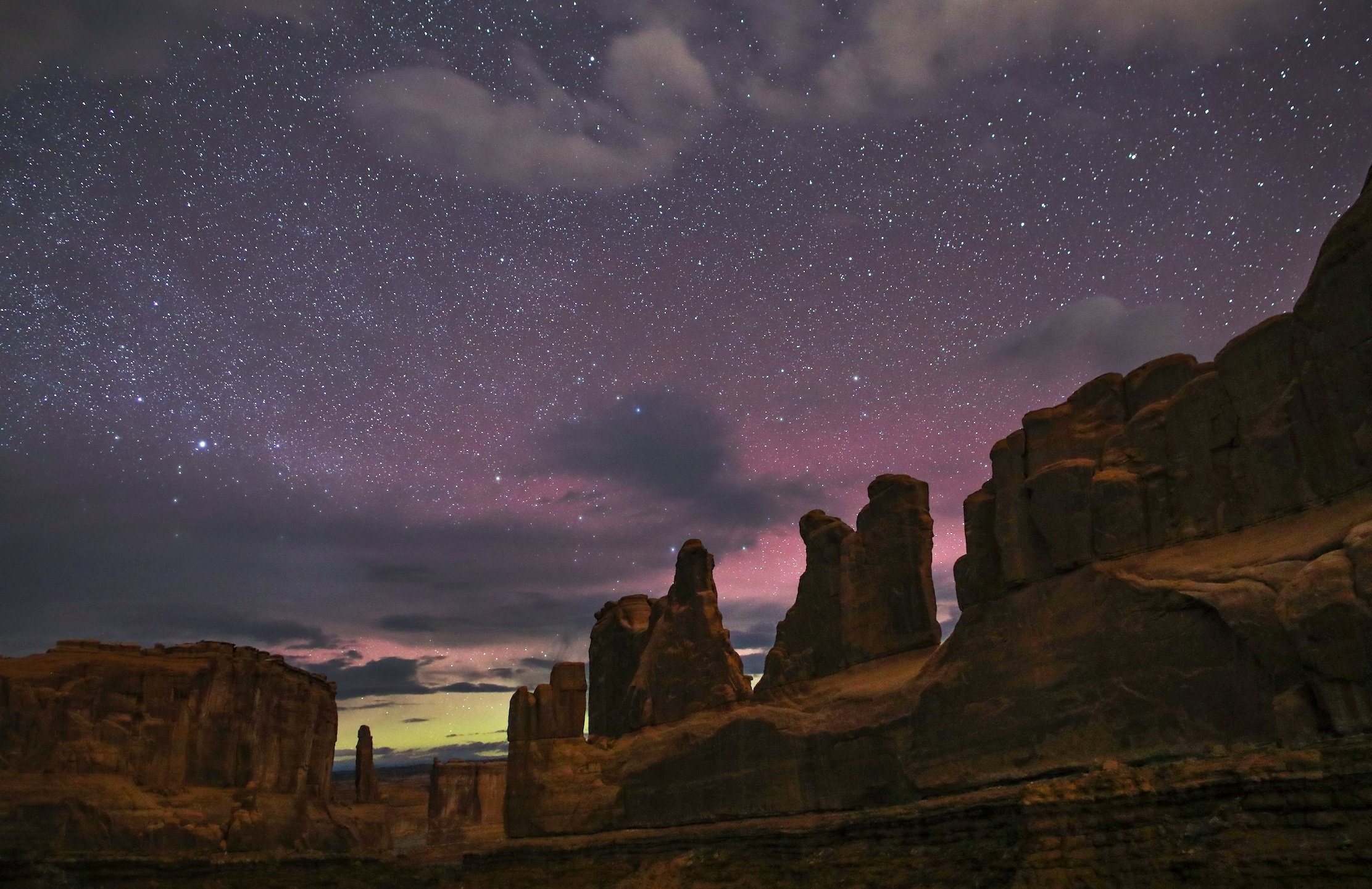 slihouetted towers of sandstone at night. in the sky is a diffuse glow of yellow and red