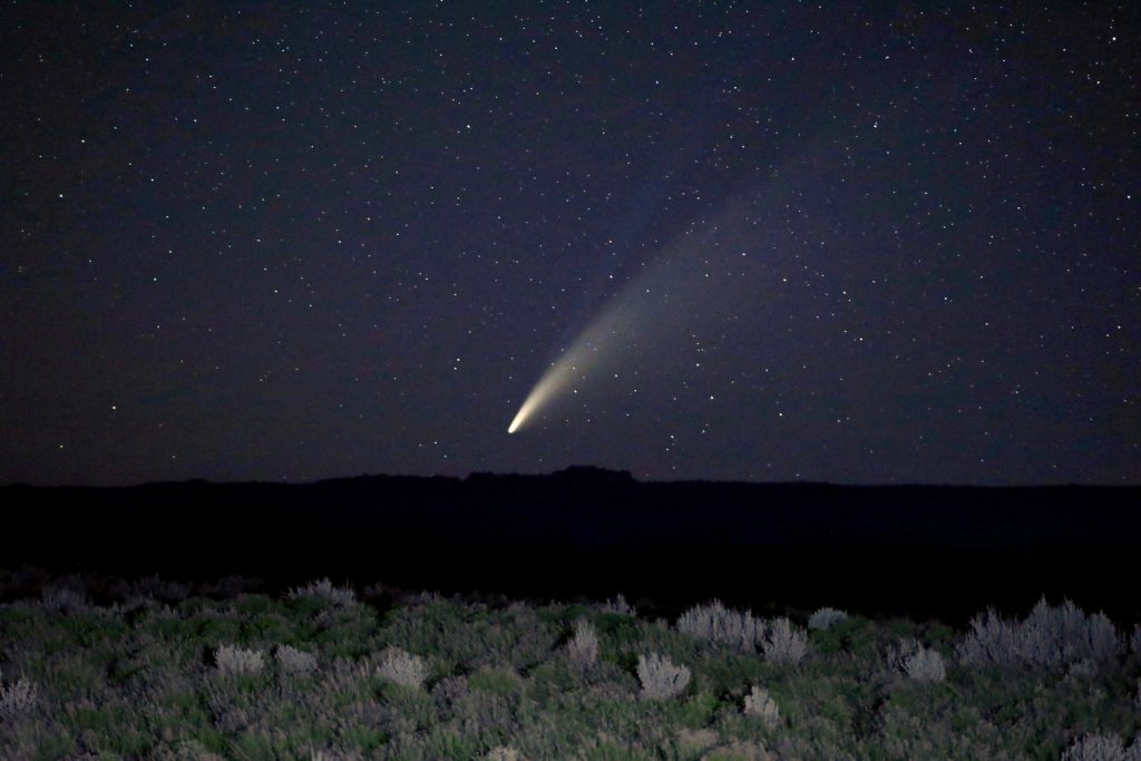 comet with long tail in the sky over a field of green sagebrush